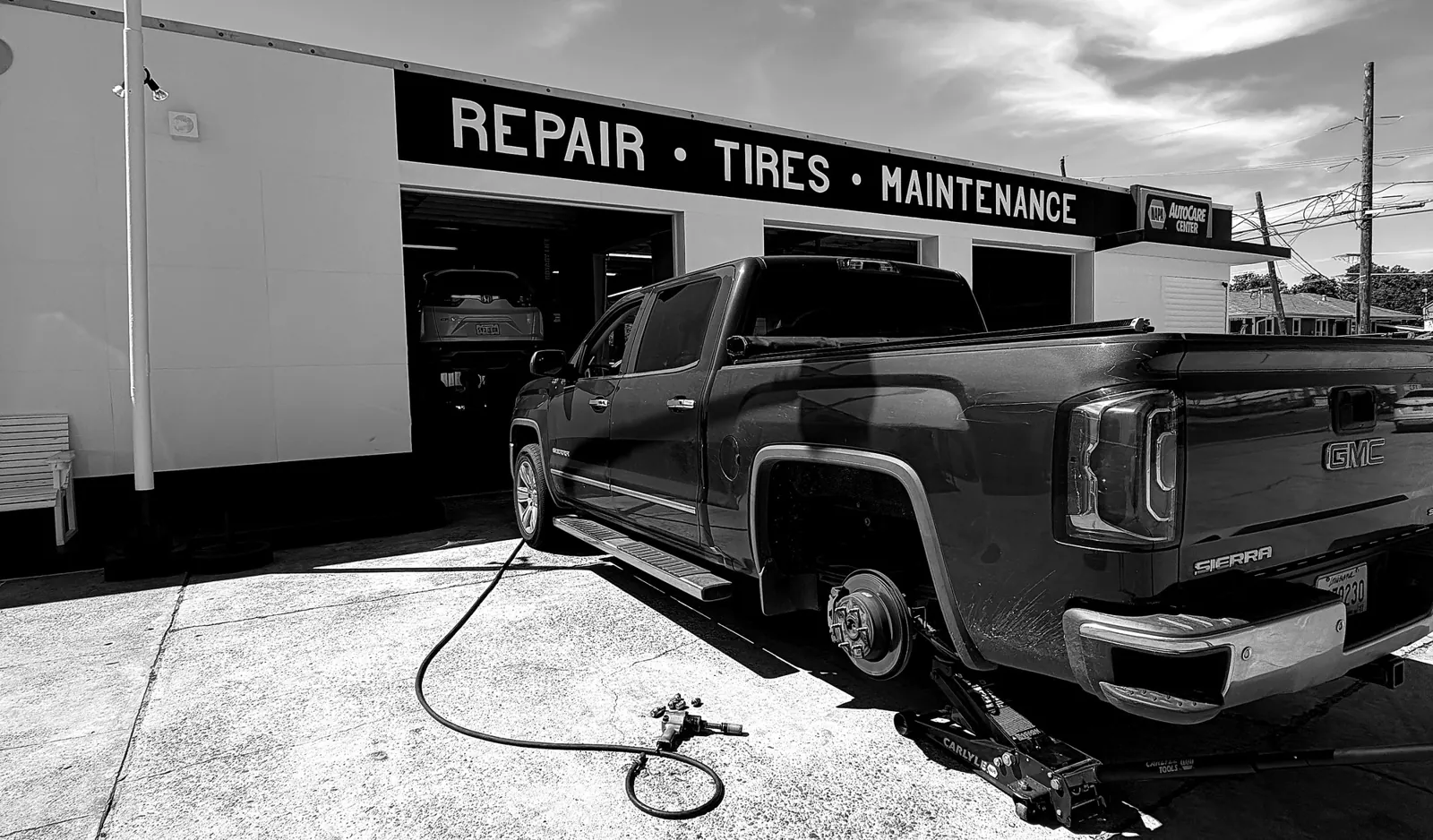ATS Auto Repair technician replacing a wheel on a GMC Sierra outside the shop, Repair Tires Maintenance sign overhead, NAPA AutoCare badge visible
