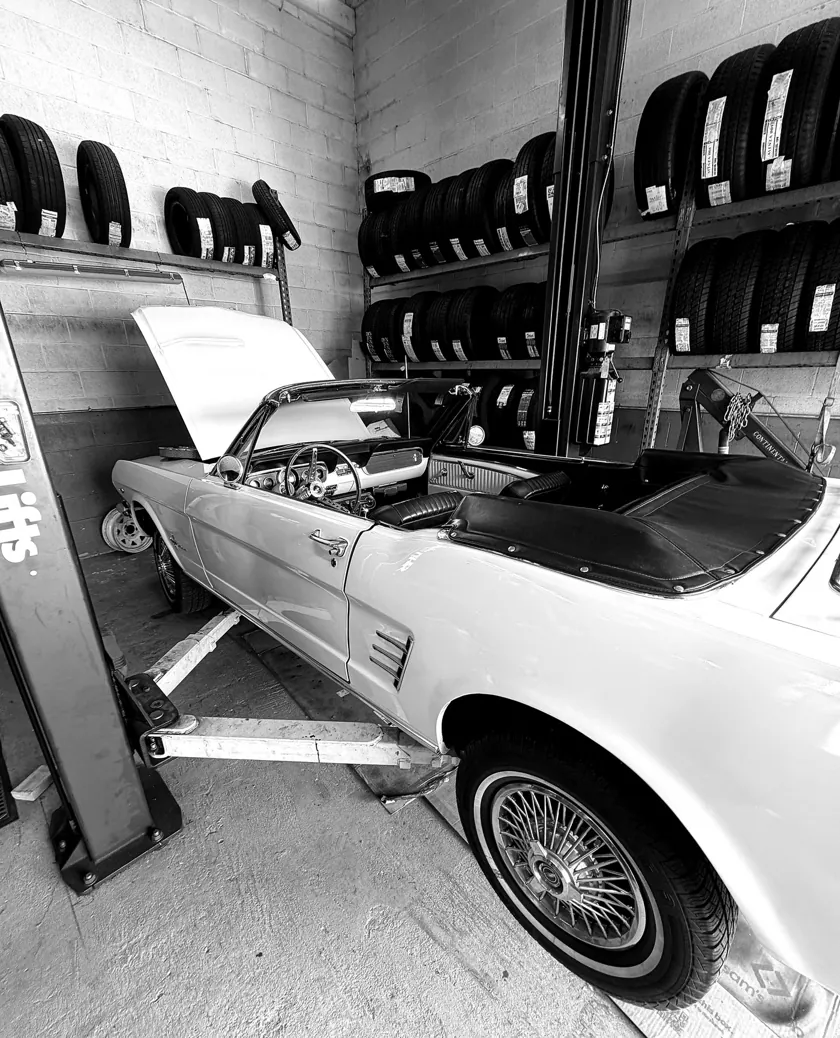 Classic Ford Mustang convertible on the ATS Auto Repair lift with tire inventory racks behind it